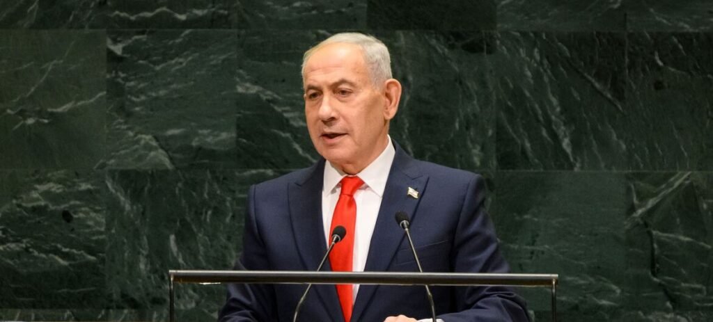 Benjamin Netanyahu in a dark suit speaking at a podium with microphones.